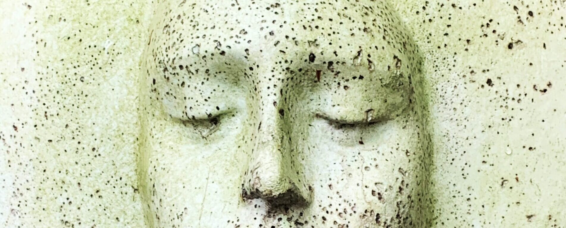 Green ceramic-like face speckled with dots with the eyes closed.
