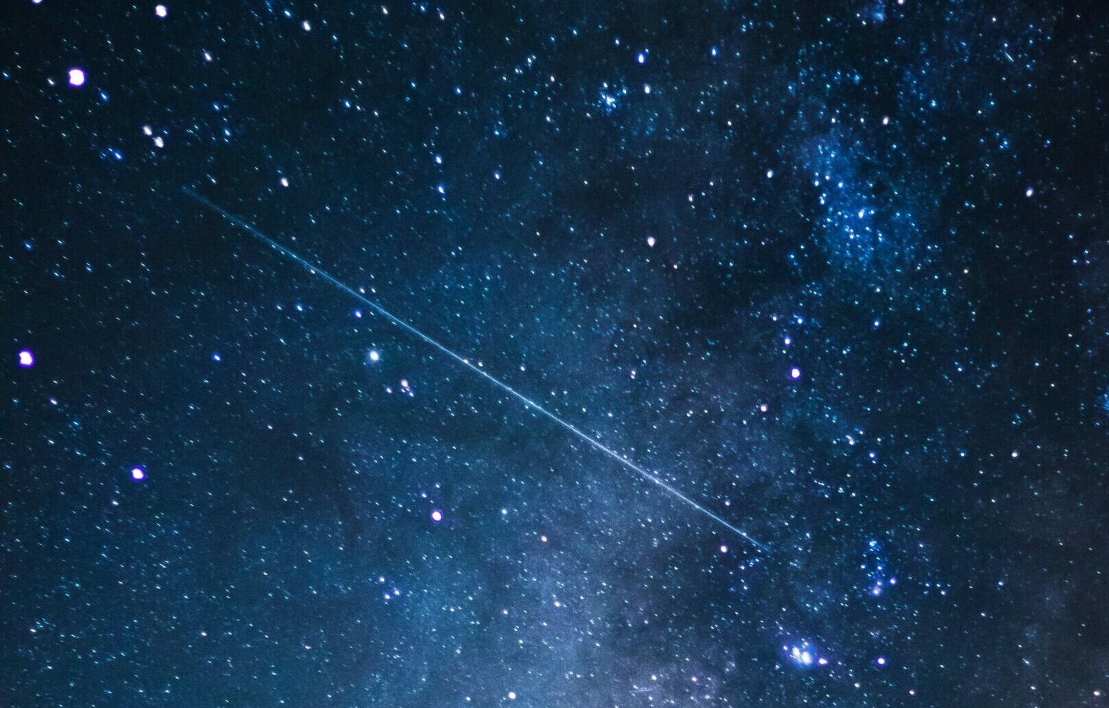 starry night sky above a forest with a shooting star