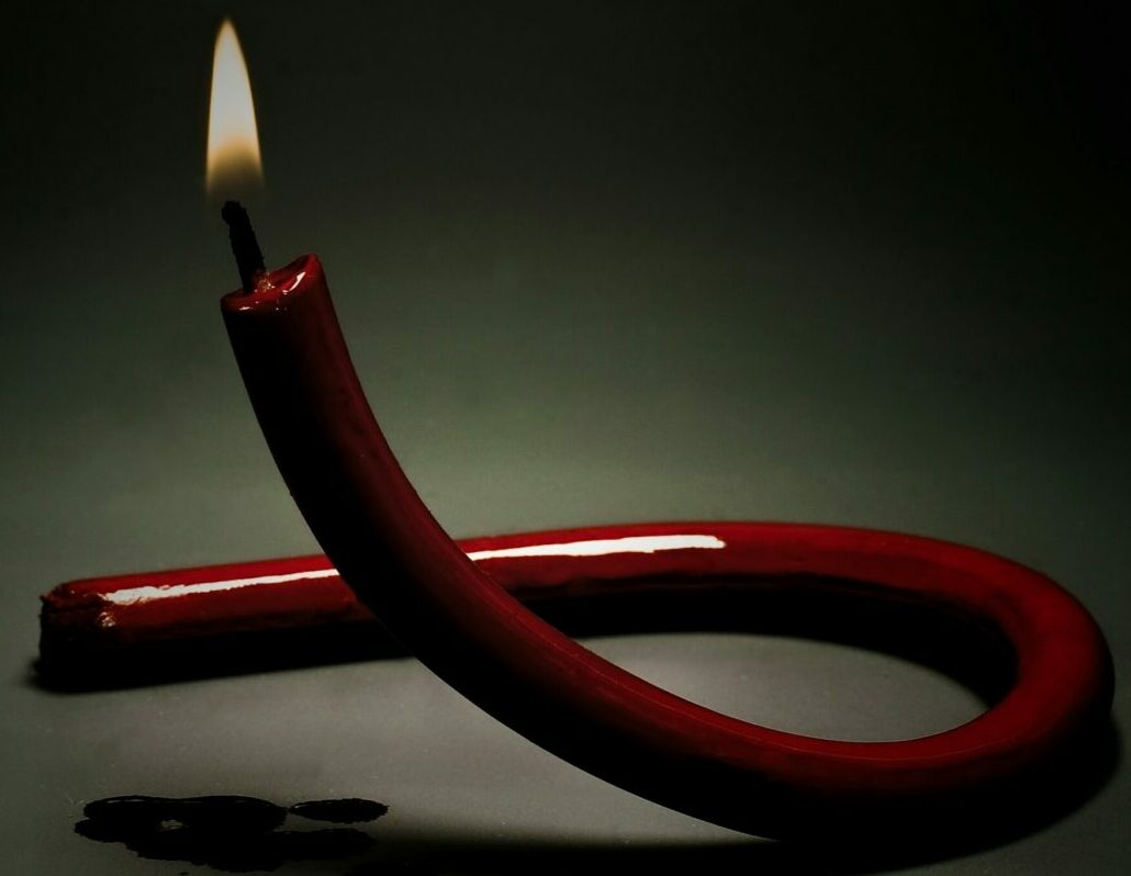 Red candle shaped as red ribbon that is lit